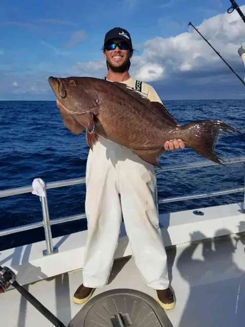 Angler holding a large snapper on the deck of a deep sea charter