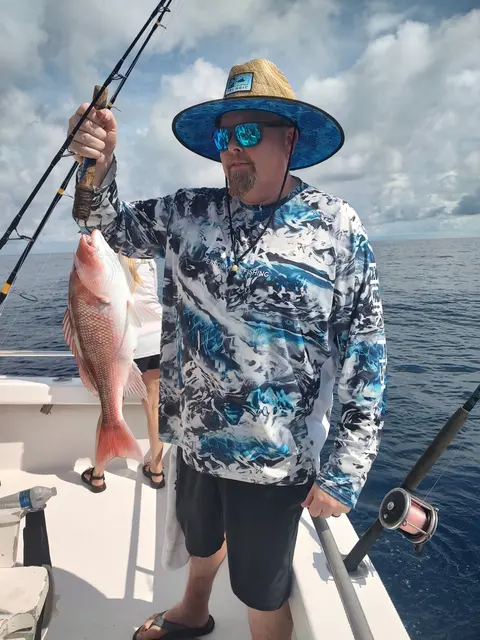 Angler in a straw hat holding up a red snapper on an offshore fishing charter