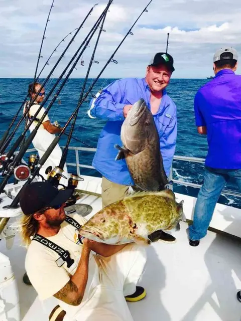 Mate and angler each holding a gag grouper on a deep sea charter
