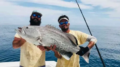 Two anglers holding a large grouper on a fishing charter in St. Augustine, FL