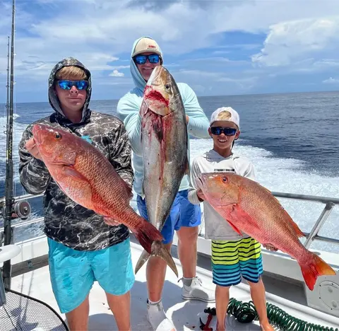 Three anglers holding red snapper and an amberjack on an offshore charter
