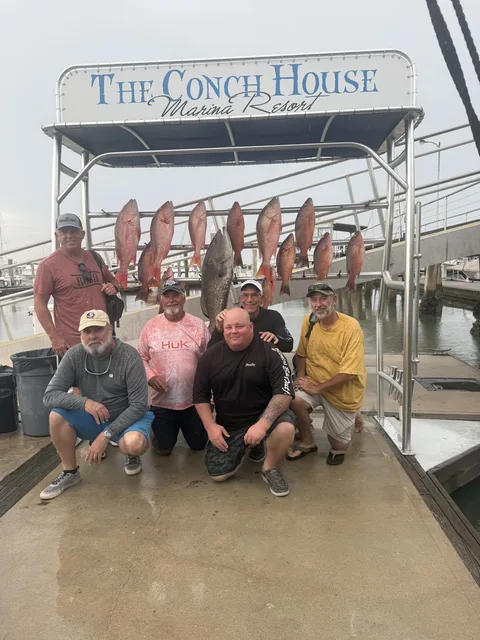 Charter group kneeling below a catch board of red snapper at The Conch House