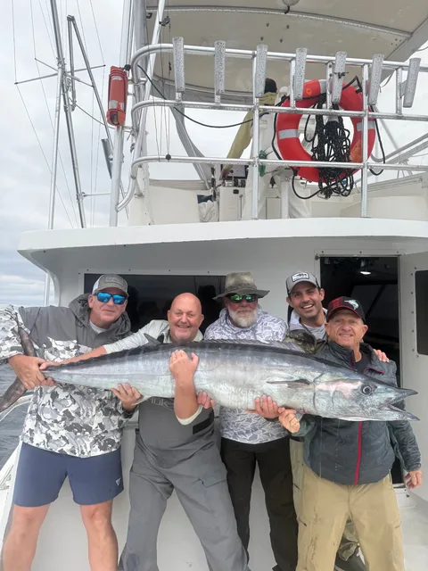 Five anglers holding a large wahoo in front of the charter boat cabin