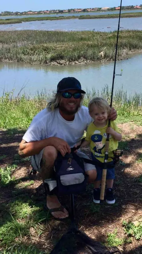 Father and toddler holding a fishing rod together beside a salt marsh