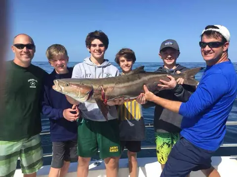 Group of kids and adults holding a cobia on a fishing charter