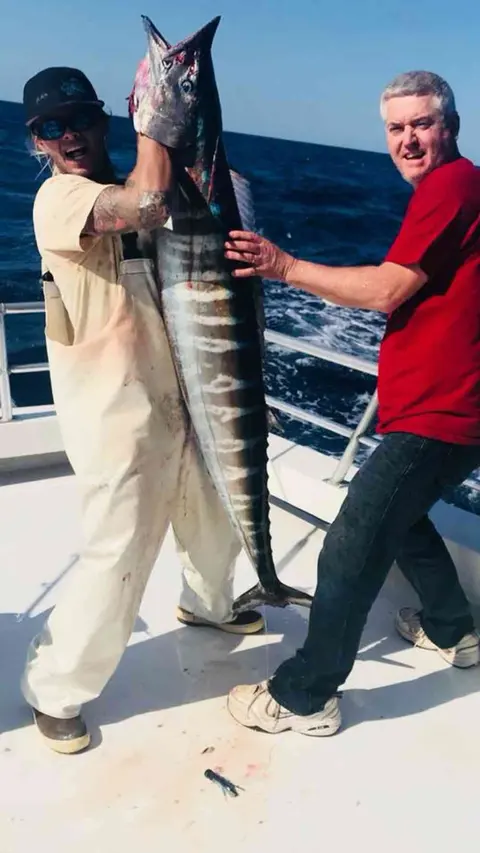 Mate and angler holding a big wahoo on deck, a charter booked from Ponte Vedra Beach, FL
