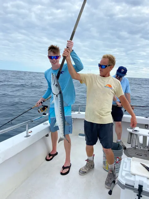 Young angler and mate lifting a barracuda on the deck of a sport fishing charter